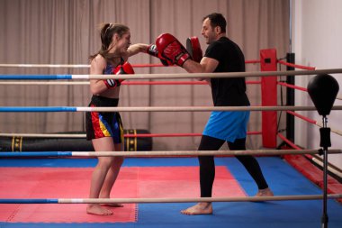 Young woman kick-box fighter doing pad work with her coach