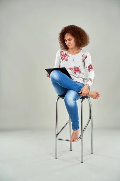 Barefoot businesswoman on a tall chair writing in a clipboard