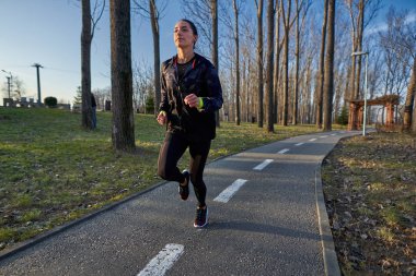 Parkta koşan eşofmanlı atletik bir kadın.
