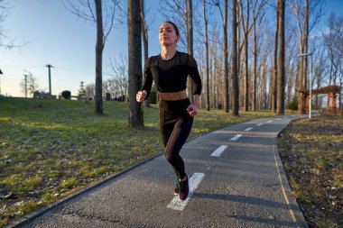 Parkta koşan eşofmanlı atletik bir kadın.