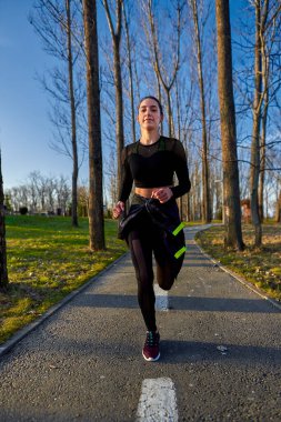 Parkta koşan eşofmanlı atletik bir kadın.