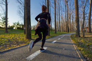 Parkta koşan eşofmanlı atletik bir kadın.