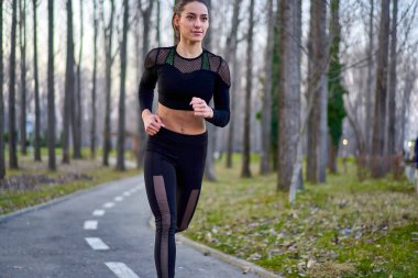 Parkta koşan eşofmanlı atletik bir kadın.