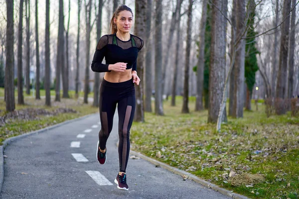 Parkta koşan eşofmanlı atletik bir kadın.