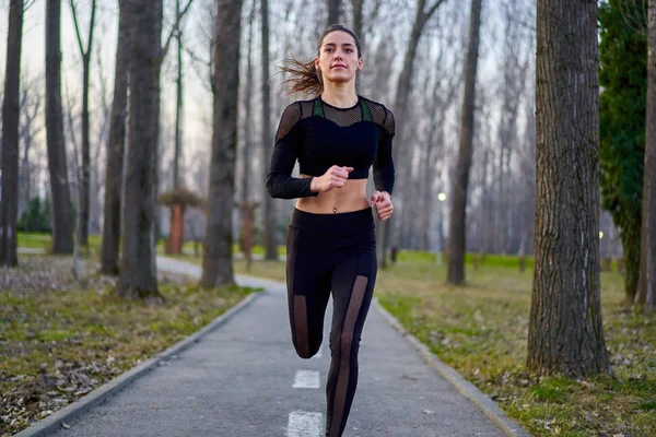 Parkta koşan eşofmanlı atletik bir kadın.