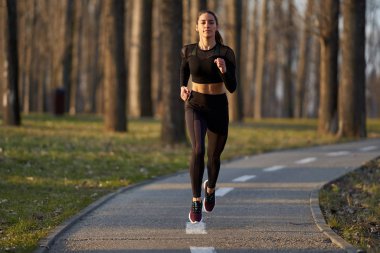 Parkta koşan eşofmanlı atletik bir kadın.