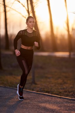 Parkta koşan eşofmanlı atletik bir kadın.