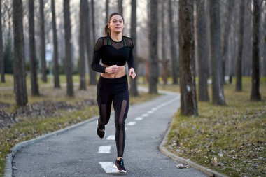 Parkta koşan eşofmanlı atletik bir kadın.