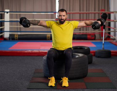 Spor salonunda dambıl egzersizi yapan atletik bir adam.