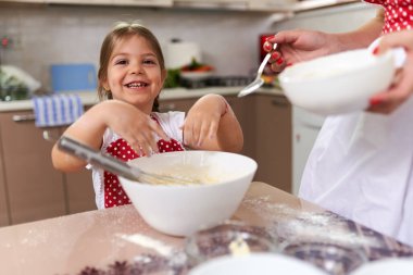 Küçük kız mutfakta annesine yardım ediyor.