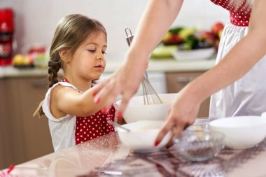 Küçük kız mutfakta annesine yardım ediyor.