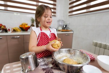 Küçük kız mutfakta hamur işi yoğuruyor.