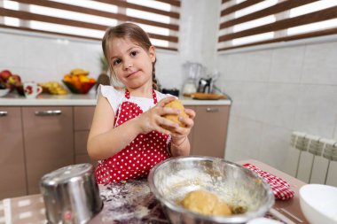 Küçük kız mutfakta hamur işi yoğuruyor.