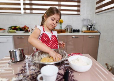 Küçük kız mutfakta hamur işi yoğuruyor.