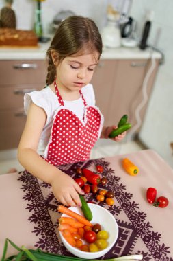 Küçük kız çeşitli sebzeleri bir kaseye yerleştiriyor.