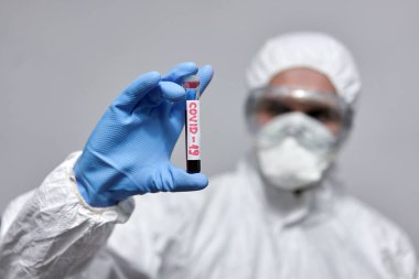 Koronavirüs için test tüpü olan koruyucu giysili bir doktor.