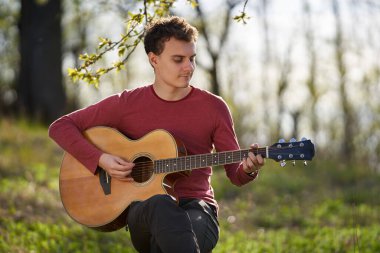 Genç adam dışarıda gitar çalıyor.