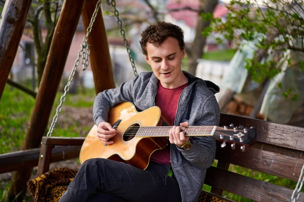 Bonito Jovem Tocando Guitarra Enquanto Sentado Swing Livre — Fotografia de Stock