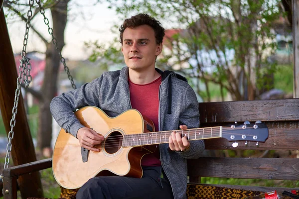 Knappe Jongeman Spelen Gitaar Terwijl Zitten Een Schommel Outdoor — Stockfoto