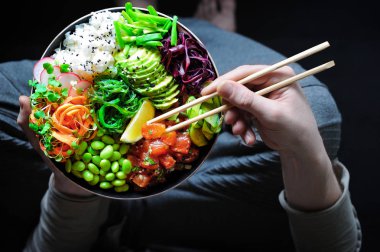 Salamura edilmiş karpuz, edamame, avokado, yosun, havuçlu erişte ve mikro yeşillik. Koşu pantolonlu bir adam tabak ve yemek çubuğu tutuyor. Sağlıklı beslenme. Vejetaryen gıda konsepti