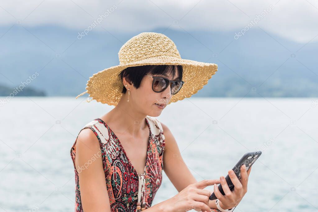 woman with hat sit at a pier using cellphone