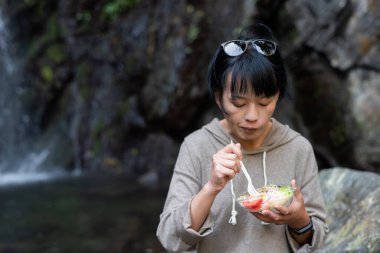 Asyalı kadın şelalenin yanında salata yiyor.