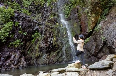 Asyalı kadın şelale yakınında bir resim çekmek