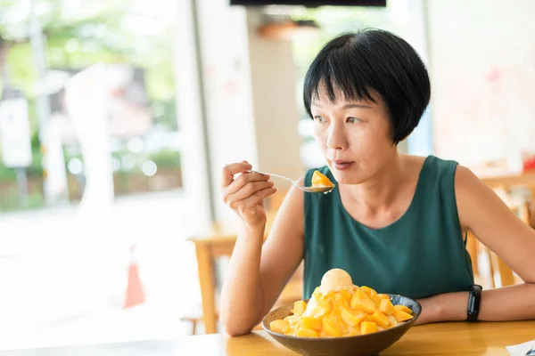 成熟したアジアの女性はマンゴーのかき氷を食べる — ストック写真