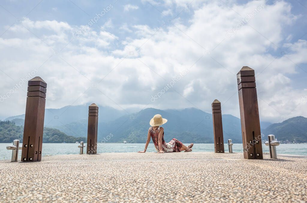 traveling Asian woman with hat sit at a pier at Sun Moon Lake, Taiwan