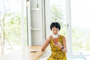 Gündüz vakti bir kafede cep telefonu kullanan bir kadın.