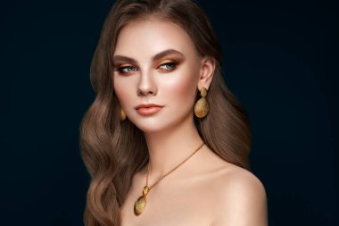 Mükemmel makyajlı esmer kız. Kıvırcık saçlı güzel bir model kadın. Bakım ve güzellik ürünleri. Modaya uygun altın makyajlı bayan. Koyu mavi arka planda mücevherleri olan bir model