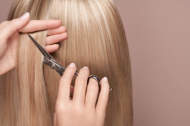 Kuaför uzun sarı saçlarını makasla keser. Kuaför, kuaför. Bakım ve güzellik ürünleri. Boyalı saç.