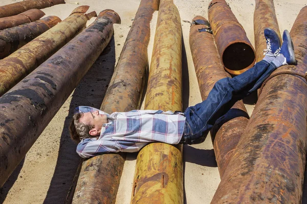 Jongeman ingedommeld, liggend op metalen buizen — Stockfoto