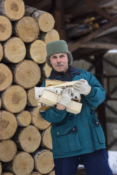 Starší muž v zimním oblečení s březovým palivem — Stock fotografie