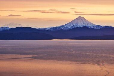 the setting sun illuminates the Vilyuchinsky volcano and part of a huge bay on the Kamchatka Peninsula clipart