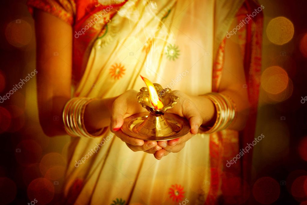 Close up Indian woman in traditional sari lighting oil lamp and celebrating Diwali or deepavali, fesitval of lights at temple. Female hands holding oil lamp.