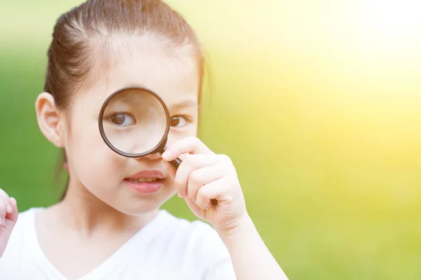 Asian kid with magnifier glass at outdoors. — Stock Photo, Image