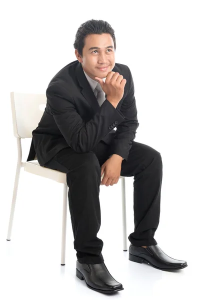 Весь азиатский бизнесмен сидит на белом стуле и думает: — стоковое фото