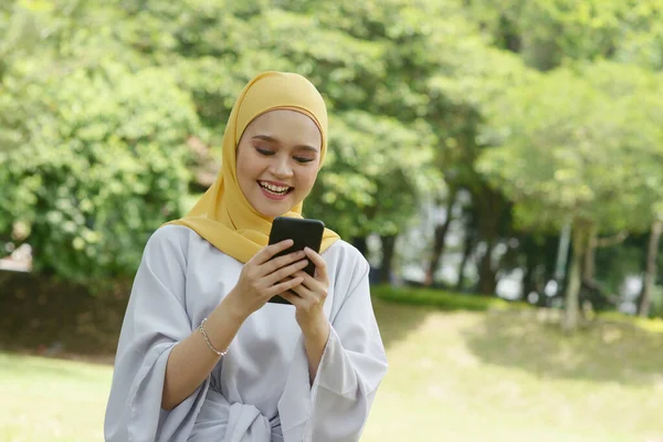 スマートフォンを使った明るいイスラム教徒の女の子の肖像 屋外で笑顔 — ストック写真