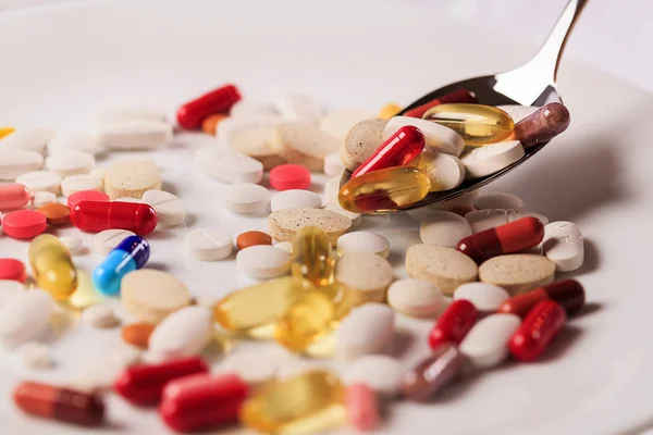 Kolorowe kapsułki i tabletki na płytce z łyżką, z bliska — Zdjęcie stockowe