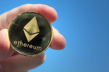 Bir altın Ethereum para tutan el. Ethereum cryptocurrency, blockchain teknoloji. Kripto para birimi Ethereum, Eth, kripto madeni para. Ethereum altın sikke mavi gökyüzü arka plan üzerinde makro çekim. Blockchain teknoloji, araştırma kavramı.