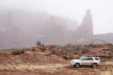Moab , UT, USA - February 9, 2020:  Toyota 4runner SUV (2016 trail edition, stock vehicle) with recovery ladders on roof racks on a 4x4 trail in winter conditions with Fisher Towers in background. clipart