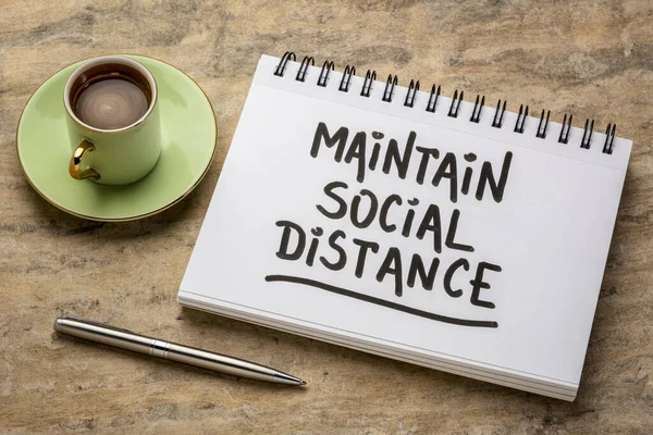 maintain social distance advice or reminder - handwriting in a spiral art sketchbook with a cup of coffee against handmade paper, infection control during covid-19 virus pandemic
