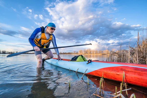 资深男子划桨手 他站在平静湖岸的划桨板上 独自划桨 与社交场合的疏远一样健康和训练有素 — 图库照片