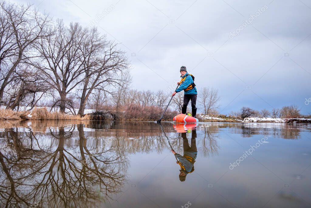 solo lake paddling as social distancing recreation during coronavirus pandemic, a senior male paddler on stand up paddleboard in early spring in Colorado