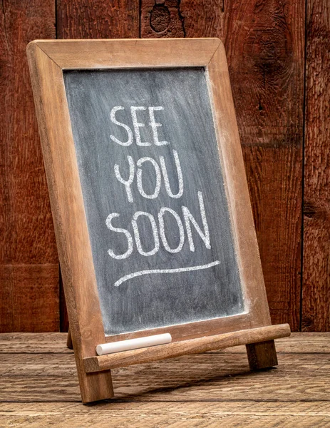 see you soon blackboard sign with white chalk smudges against rustic barn wood, business invitation concept