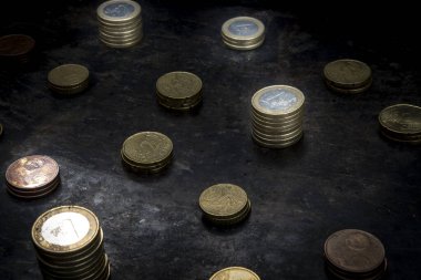 Yırtık metal detayları olan koyu siyah bir zemin üzerinde Avro sikkelerinden oluşan düzenli bir mozaik.