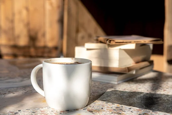 white cup with cappuccino coffee and books on an old table with a background of old rustic woods