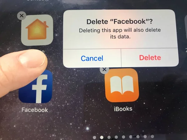Imagen macro de un dedo a punto de eliminar la aplicación de Facebook de una pantalla de iPad - puede ser debido a problemas de privacidad de datos, Facebook se enfrenta actualmente —  Fotos de Stock