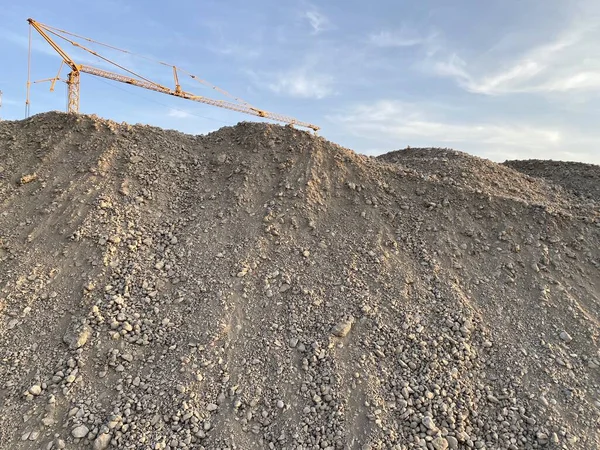 Large gravel mound with construction crane in the background — Stock Photo, Image